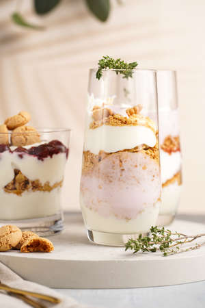 Three glasses with a layered creamy yoghurt dessert trifle with cookies, amaretti, cherries and thyme in a tropical settingの写真素材