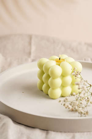One white square bubble candle on a concrete tray on a linen table cloth with a blooming branchの写真素材
