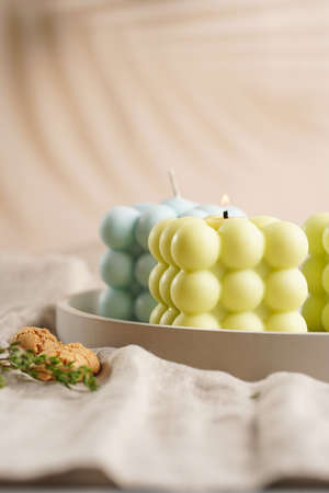 Green, blue and white square bubble candles on a concrete tray on a linen table clothの写真素材