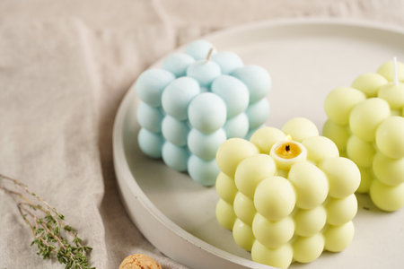 Green, blue and white square bubble candles on a concrete tray on a linen table clothの写真素材