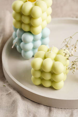 Green, blue and white square bubble candles on a concrete tray on a linen table cloth with thyme and blooming branchesの写真素材