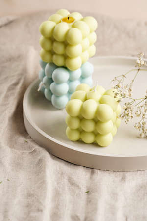 Green, blue and white square bubble candles on a concrete tray on a linen table cloth with thyme and blooming branchesの写真素材