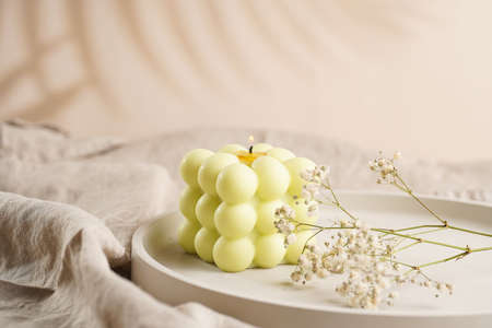 One white square bubble candle on a concrete tray on a linen table cloth with a blooming branchの写真素材