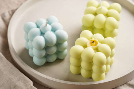 Green, blue and white square bubble candles on a concrete tray on a linen table clothの写真素材