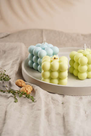 Green, blue and white square bubble candles on a concrete tray on a linen table clothの写真素材