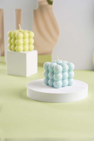 One blue square bubble candle on a white oval and an off-white candle on a cube in the backの写真素材
