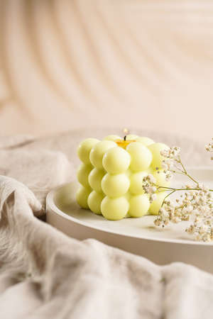 One white square bubble candle on a concrete tray on a linen table cloth with a blooming branchの写真素材