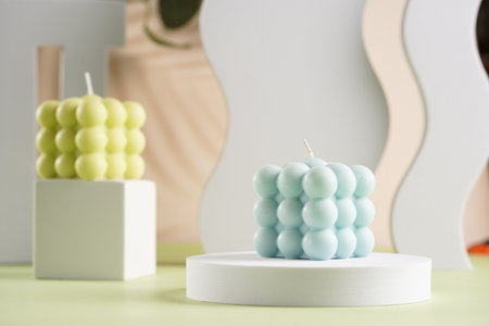 One blue square bubble candle on a white oval on a pastel green surfaceの写真素材