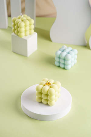 Three blue, green and white square bubble candles on a pastel green surfaceの写真素材