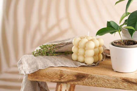 An off-white square bubble candle on a linen cloth on a rustic wooden table with plants at a tropical settingの写真素材