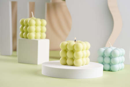 Three blue, green and white square bubble candles on a pastel green surfaceの写真素材