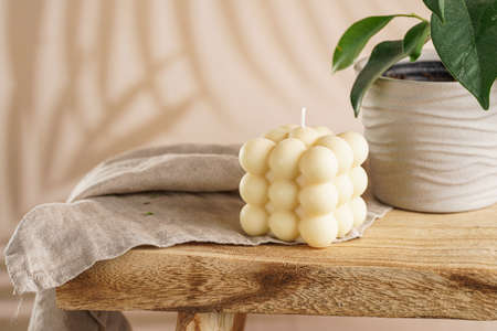 An off-white square bubble candle on a linen cloth on a rustic wooden table with plants at a tropical settingの写真素材