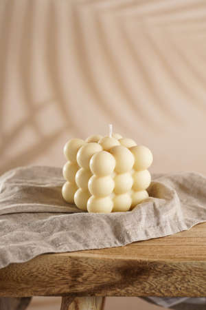 An off-white square bubble candle on a linen cloth on a rustic wooden table in a tropical settingの写真素材
