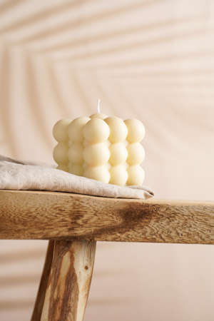 An off-white square bubble candle on a linen cloth on a rustic wooden table in a tropical settingの写真素材