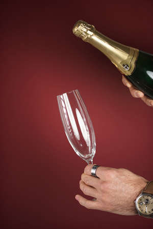 Male hands holding a champagne glass and an uncorked champagne bottle on burgundy backgroundの写真素材