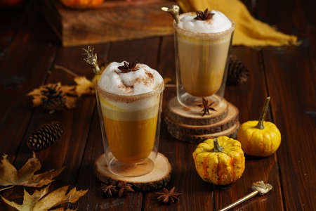 Two glasses of an orange pumpkin spice latte coffee drink with whipped cream, brass drinking straw and cinnamon sprinklesの写真素材