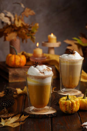 Two glasses of an orange pumpkin spice latte coffee drink with whipped cream, brass drinking straw and cinnamon sprinklesの写真素材