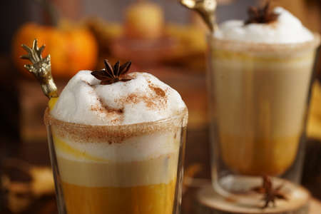 Two glasses of an orange pumpkin spice latte coffee drink with whipped cream, brass drinking straw and cinnamon sprinklesの写真素材