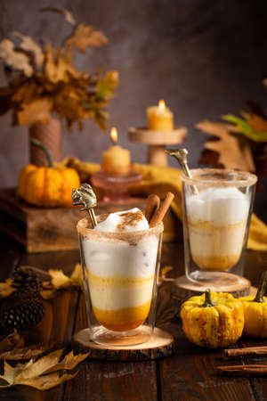 Two glasses of an orange pumpkin spice latte coffee drink with whipped cream, brass drinking straw and cinnamon sprinklesの写真素材