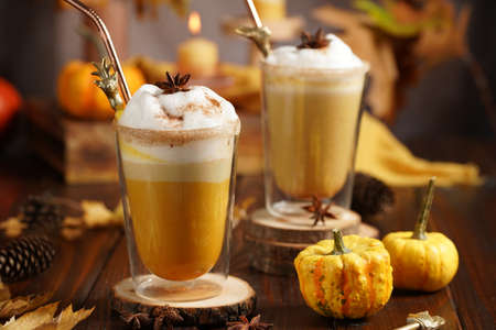 Two glasses of an orange pumpkin spice latte coffee drink with whipped cream, brass drinking straw and cinnamon sprinklesの写真素材