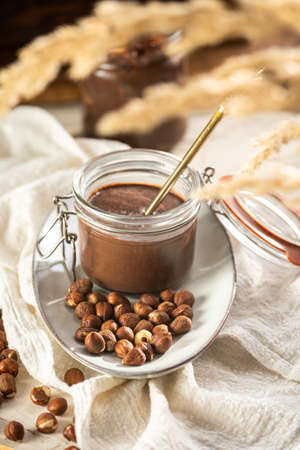 Homemade hazelnut cocoa chocolate cream in mason jar on plate surrounded by hazelnutsの写真素材