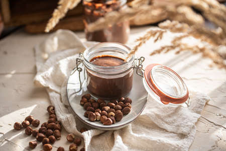 Homemade hazelnut cocoa chocolate cream in mason jar on plate surrounded by hazelnutsの写真素材