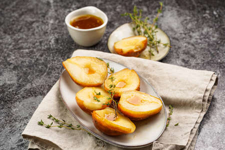 Caramelized pear halves on an oval gray plate with thyme branches and caramel on a concrete gray table surfaceの写真素材