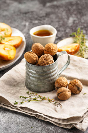 A metal mug with whole brown walnuts on a beige colored linen cloth, caramelized pears and thyme branches on a gray concrete surfaceの写真素材