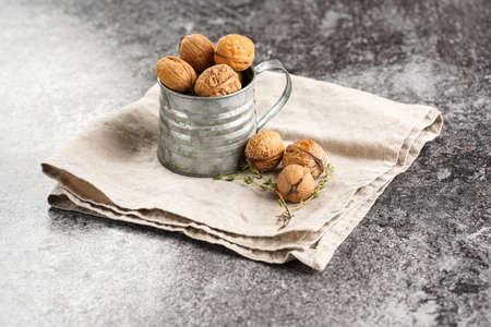 A metal mug with whole brown walnuts on a beige colored linen cloth on a gray concrete surfaceの写真素材