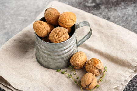 A metal mug with whole brown walnuts on a beige colored linen cloth on a gray concrete surfaceの写真素材