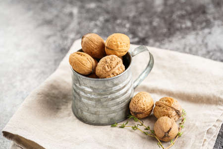 A metal mug with whole brown walnuts on a beige colored linen cloth on a gray concrete surfaceの写真素材