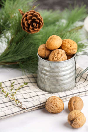 A metal mug with whole brown walnuts on a checkered linen cloth and a christmas fair-tree branch on a white table surfaceの写真素材