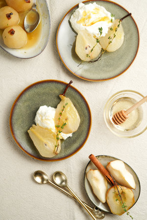 Caramelized pear halves with whipped cream on an green plates with thyme branches and caramel on a linen clothの写真素材