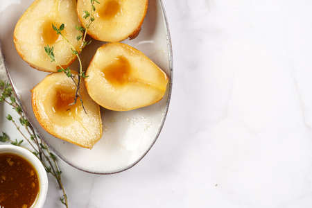 Caramelized pear halves on an oval gray plate with thyme branches and caramel on a white table surfaceの写真素材