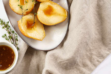 Caramelized pear halves on an oval gray plate with thyme branches and caramel on a white table surfaceの写真素材