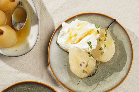 Caramelized pear halves with whipped cream on an green plates with thyme branches and caramel on a linen clothの写真素材