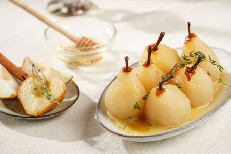 Peeled poached pears with caramel sauce on a white oval plate on a white table surfaceの写真素材