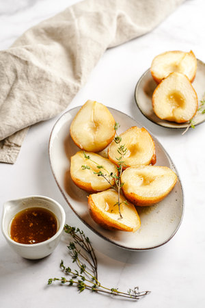 Caramelized pear halves on an oval gray plate with thyme branches and caramel on a white table surfaceの写真素材