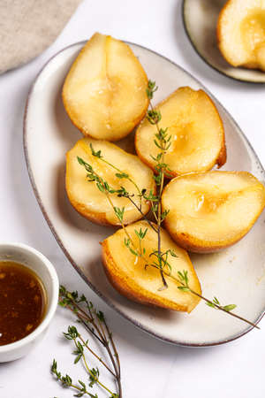 Caramelized pear halves on an oval gray plate with thyme branches and caramel on a white table surfaceの写真素材
