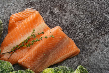 Two red raw salmon steaks and broccoli on a gray marble surface, top view, negative spaceの写真素材