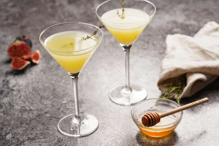 Two martini glasses with yellow non-alcoholic beverage lemonade with thyme branch, honey and figs on gray marble surfaceの写真素材