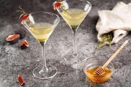 Two martini glasses with alcoholic beverage liquor with thyme branch, honey and figs on gray marble surfaceの写真素材