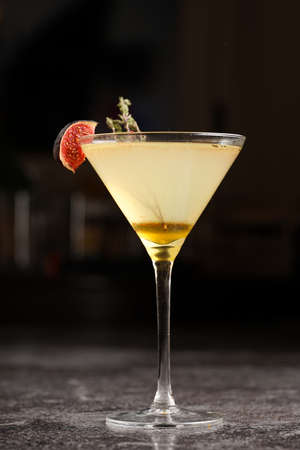 One martini glass with yellow alcoholic beverage liquor with thyme branch, honey and figs on gray table, dark bar backgroundの写真素材