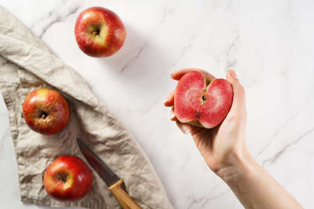 A female hand holding a half of an apple with red flesh on a marble surfaceの写真素材