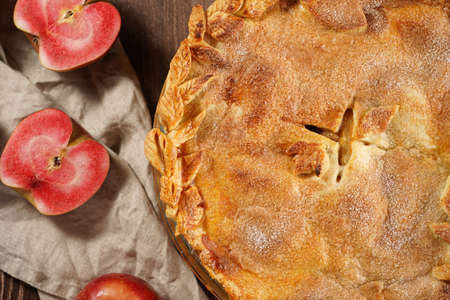 Classic traditional cinnamon apple pie and red flesh apples on a wooden table, top viewの写真素材