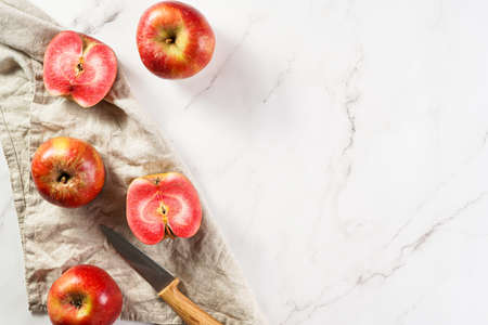 Several whole and cut apples and apple halves with red flesh and a knife on a linen cloth on a marble table, top view, negative spaceの写真素材