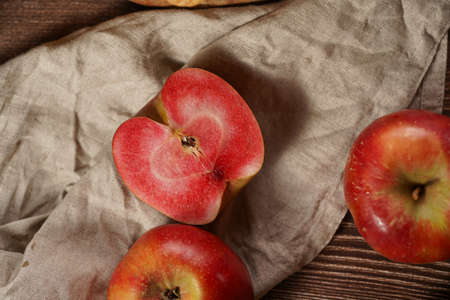 Several whole and cut apples and apple halves with red flesh on a linen cloth on a wooden tableの写真素材