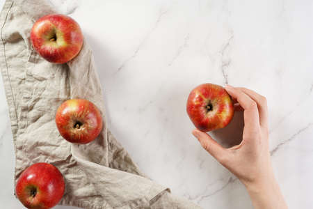 A female hand holding an apple with red flesh on a marble surfaceの写真素材
