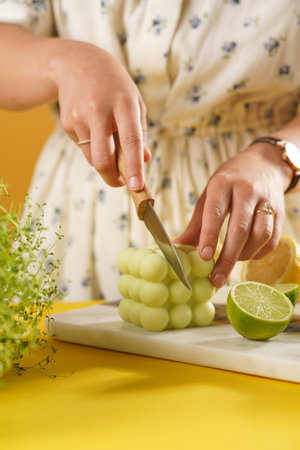 Female hands about to cut a bright green bubble candle surrounded by lemon and lime halves, fresh thymeの写真素材