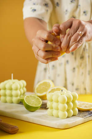 Female hands pressing lemon juice on a bright green bubble candle surrounded by lemon and lime halves, fresh thymeの写真素材